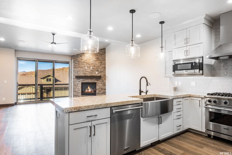 Kitchen with dark wood-type flooring, appliances with stainless steel finishes, tasteful backsplash, a fireplace, and wall chimney exhaust hood