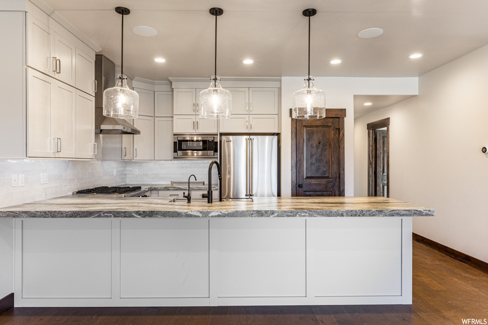Kitchen with tasteful backsplash, hanging light fixtures, white cabinetry, dark hardwood / wood-style flooring, and appliances with stainless steel finishes