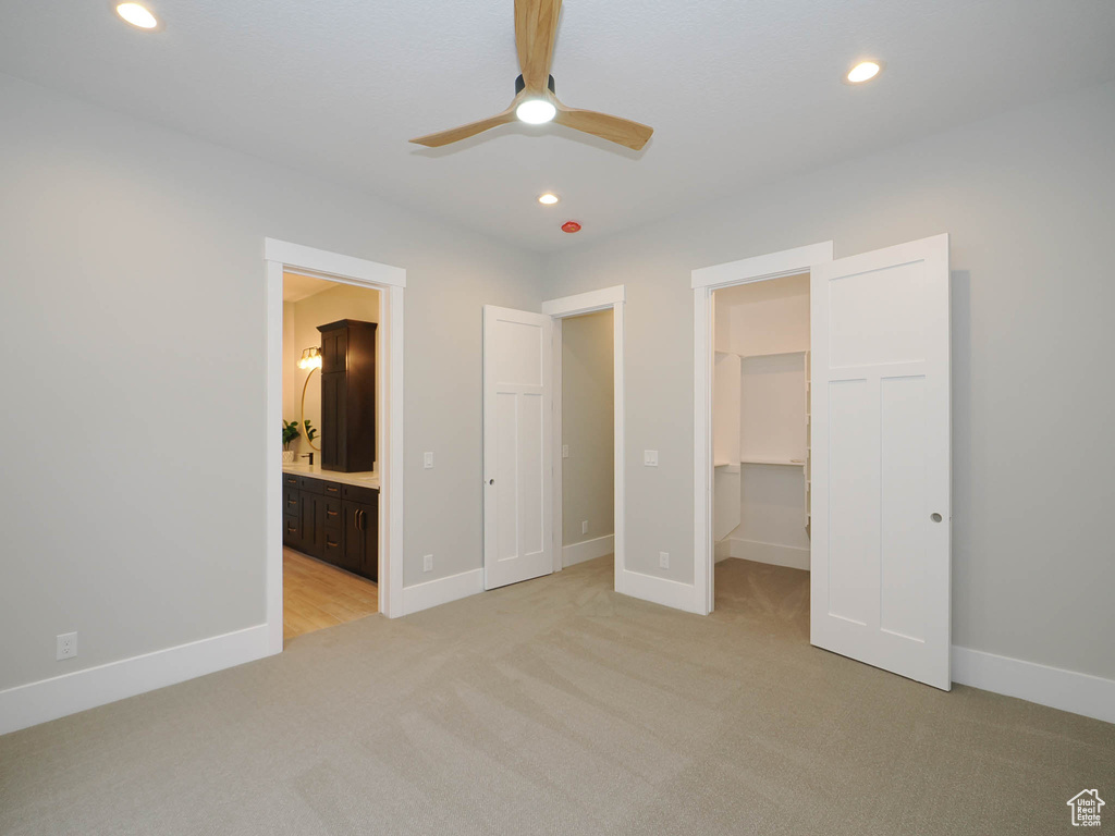 Unfurnished bedroom with ensuite bath, a closet, light carpet, a walk in closet, and ceiling fan