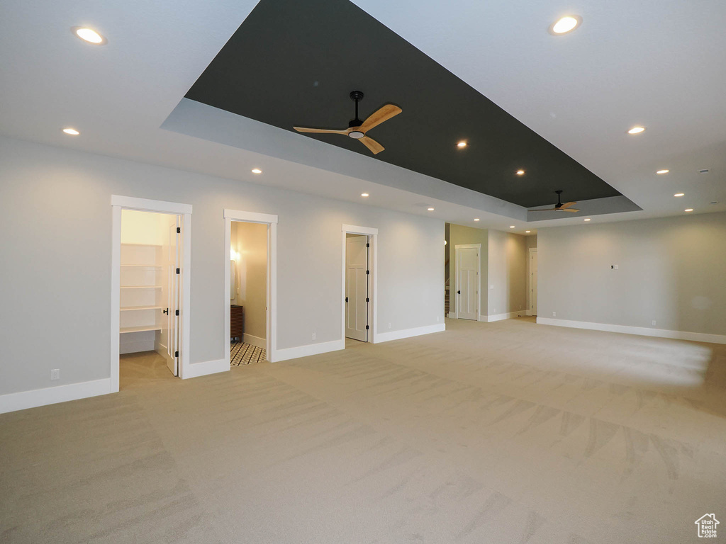 Empty room featuring a tray ceiling, ceiling fan, and light colored carpet