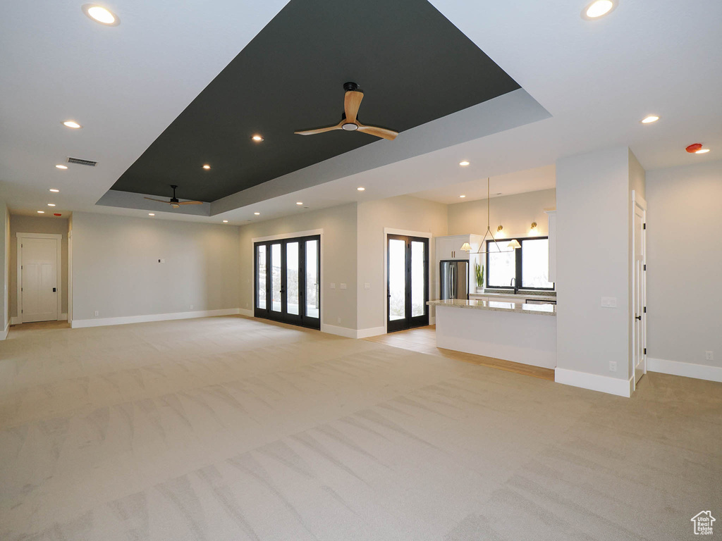Unfurnished living room featuring a tray ceiling, ceiling fan, and light carpet