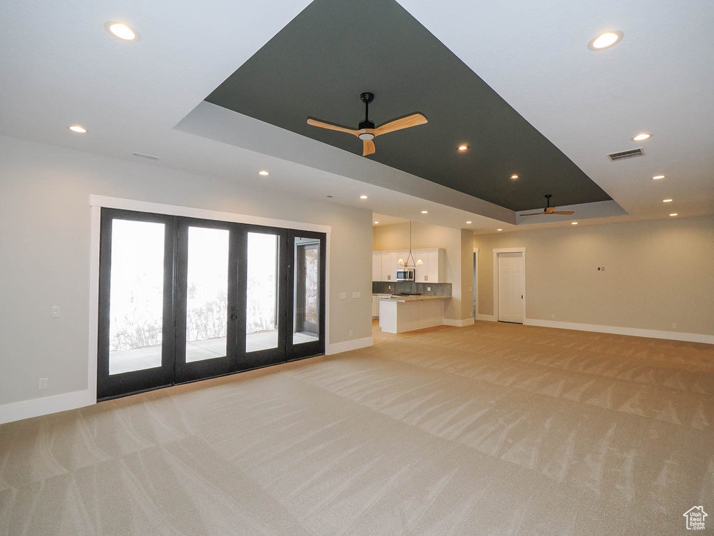 Unfurnished living room featuring a raised ceiling, light colored carpet, ceiling fan, and french doors