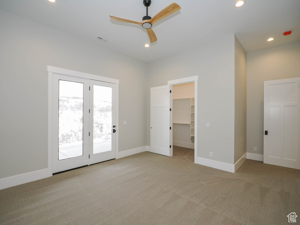 Unfurnished bedroom featuring a walk in closet, ceiling fan, light colored carpet, and access to exterior