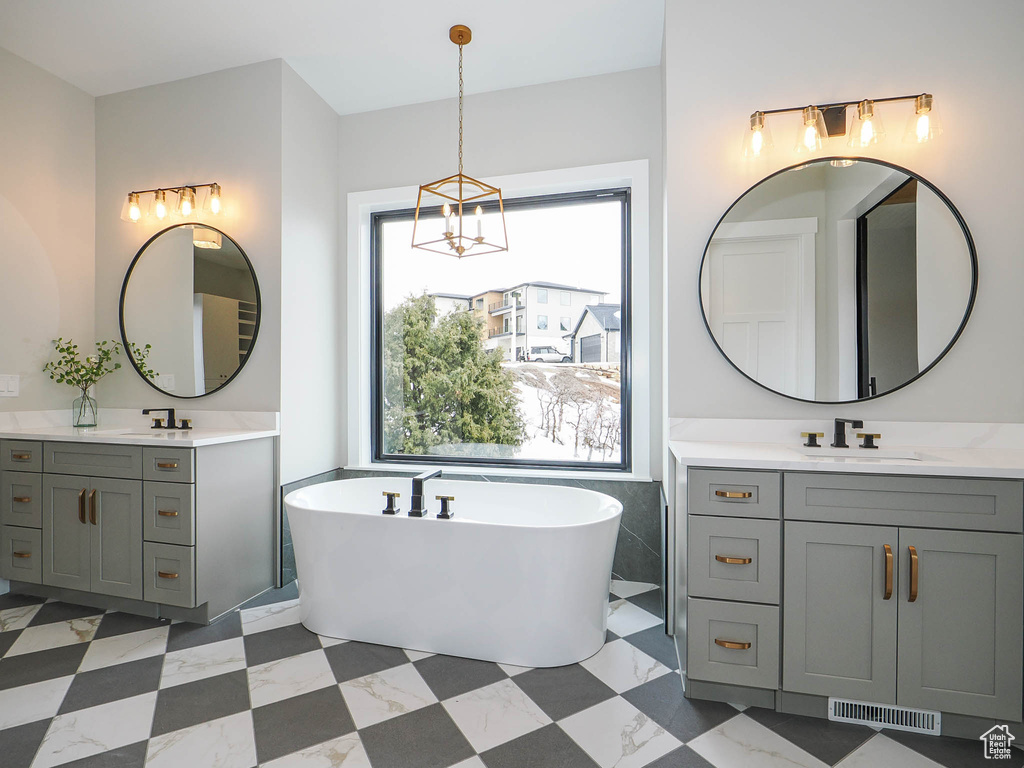 Bathroom with an inviting chandelier, a wealth of natural light, double vanity, and tile flooring