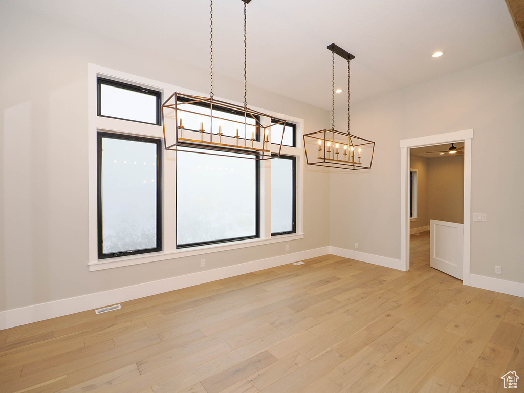 Empty room featuring plenty of natural light, ceiling fan with notable chandelier, and light wood-type flooring