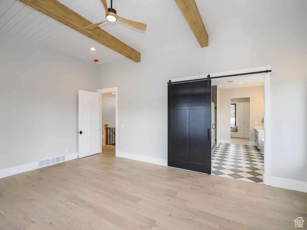 Unfurnished bedroom with a barn door, ceiling fan, connected bathroom, and light hardwood / wood-style floors
