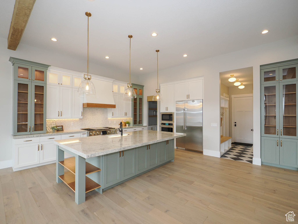 Kitchen featuring white cabinetry, a center island with sink, and built in appliances
