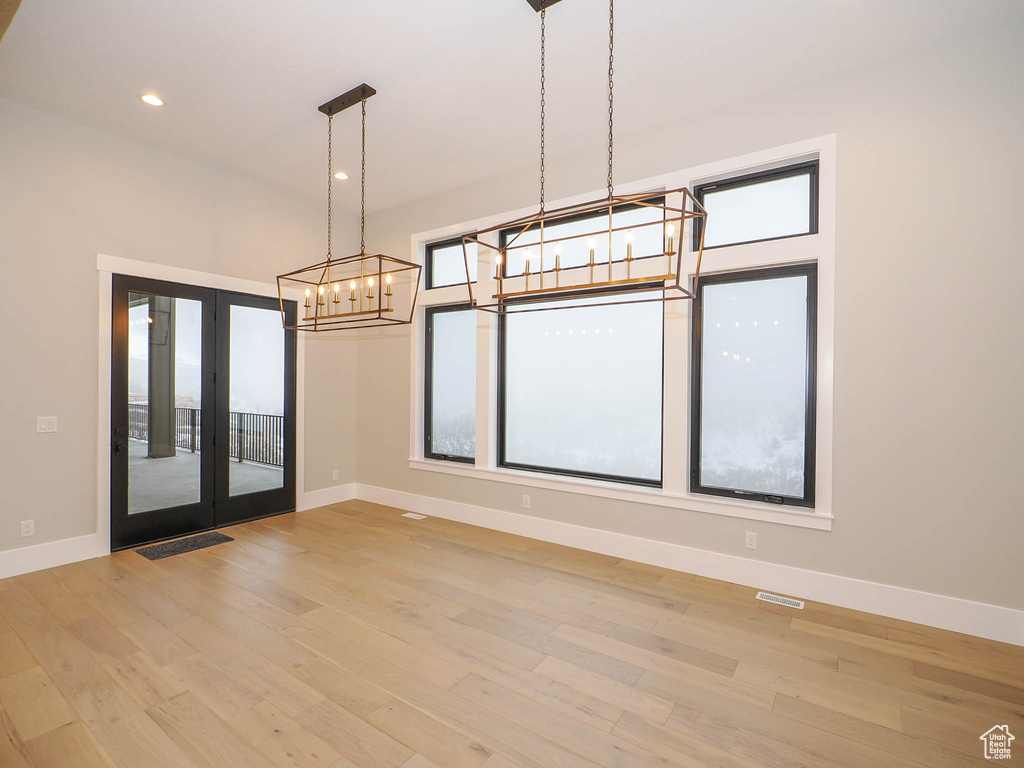 Unfurnished room with light hardwood / wood-style floors, a notable chandelier, and french doors
