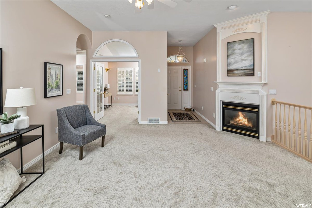 Living area with ceiling fan, a fireplace, and light colored carpet