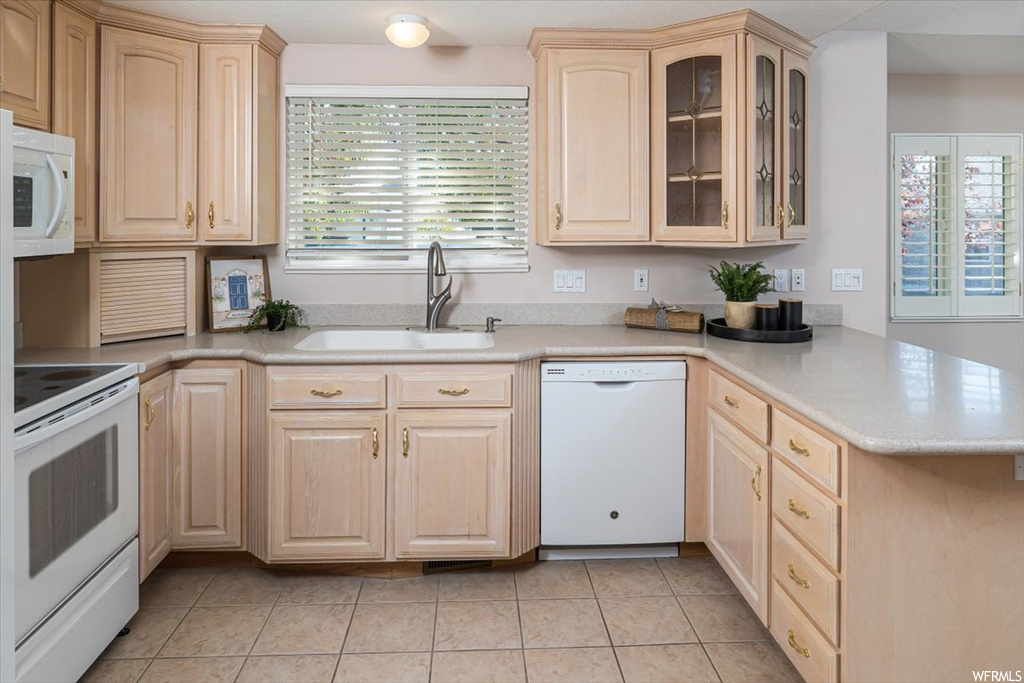 Kitchen featuring white appliances, kitchen peninsula, light tile floors, and sink
