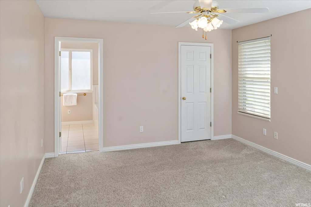 Unfurnished bedroom featuring multiple windows, ceiling fan, light carpet, and ensuite bath