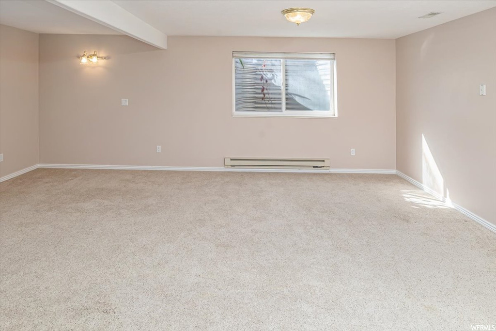 Empty room featuring light carpet, beamed ceiling, and a baseboard radiator