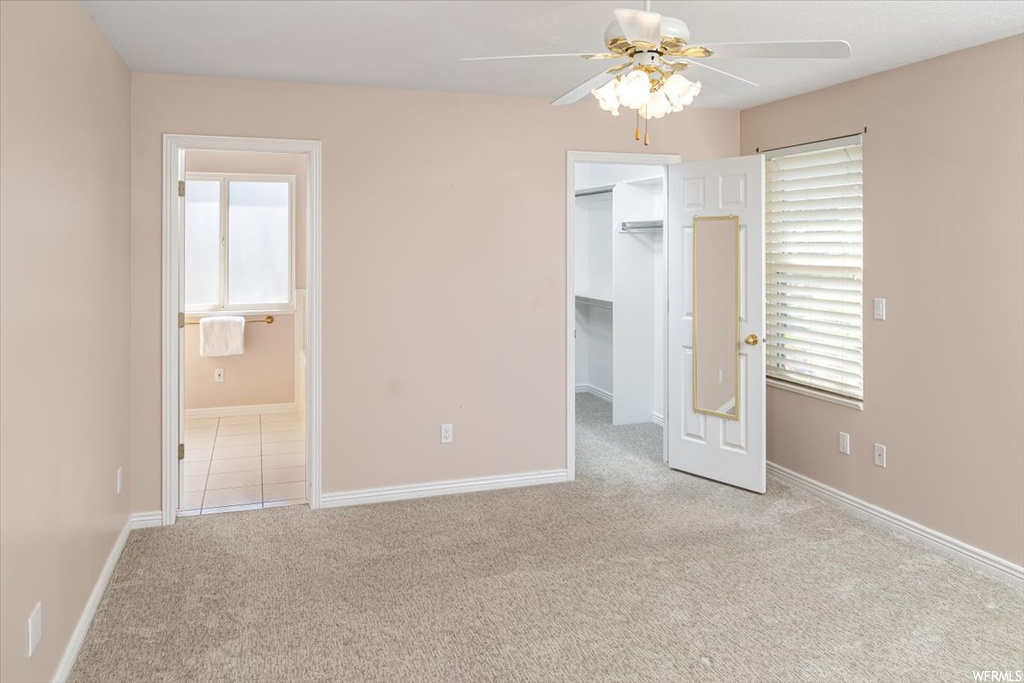 Unfurnished bedroom with a walk in closet, a closet, light tile floors, ceiling fan, and ensuite bathroom