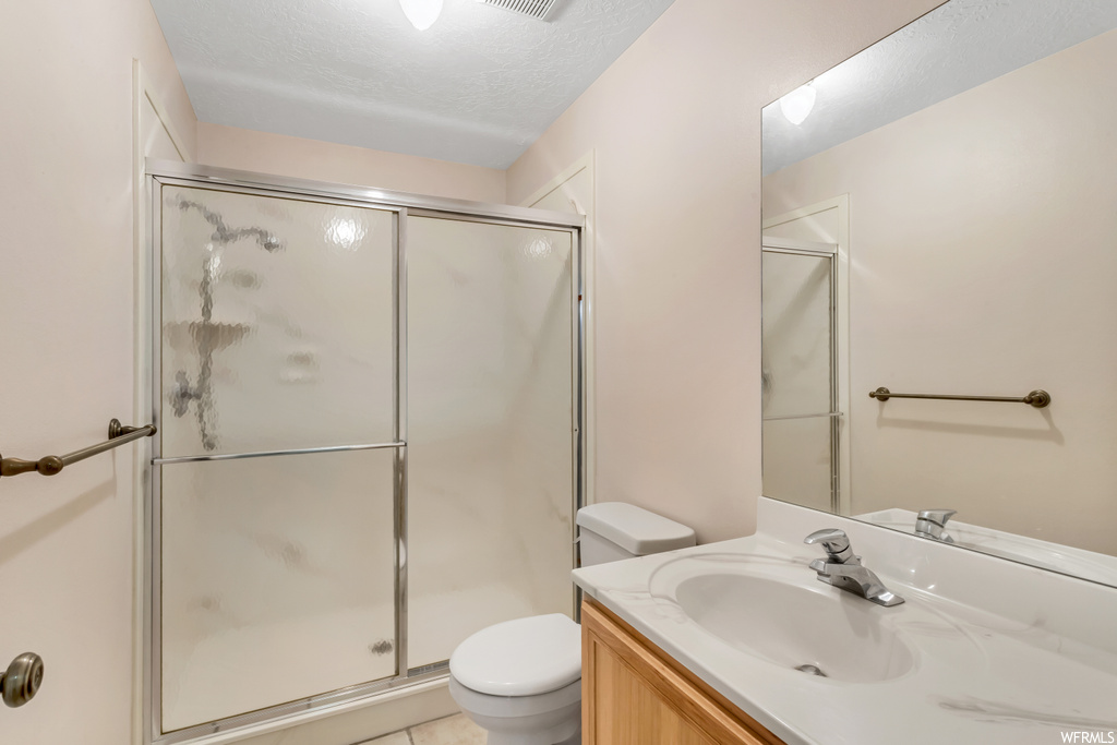Bathroom featuring vanity, tile flooring, a textured ceiling, toilet, and a shower with door