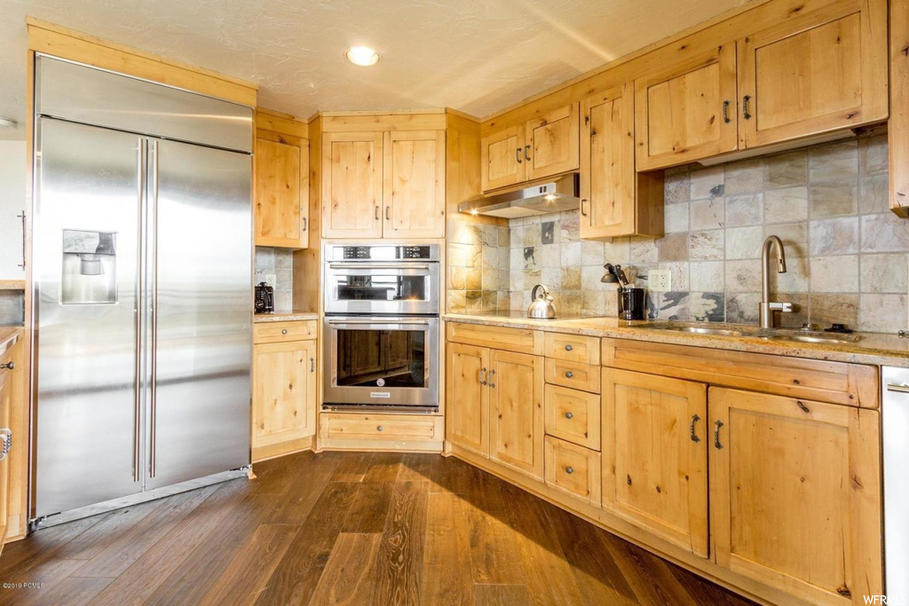 Kitchen featuring sink, wall chimney range hood, backsplash, dark hardwood / wood-style flooring, and stainless steel appliances