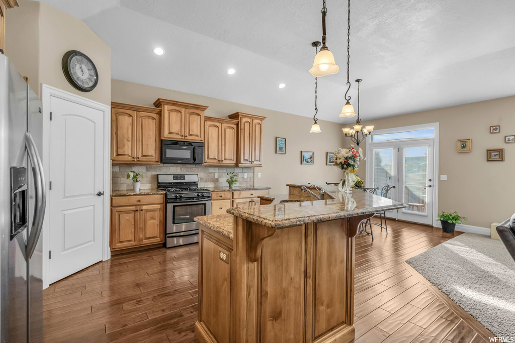 Kitchen featuring dark hardwood / wood-style floors, appliances with stainless steel finishes, an island with sink, hanging light fixtures, and a kitchen breakfast bar