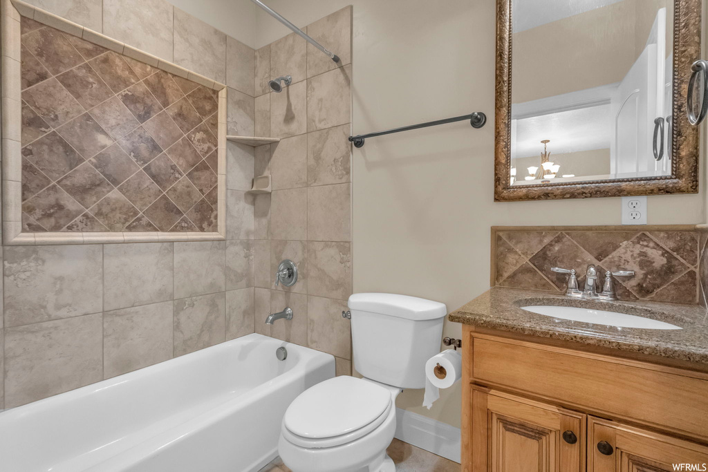 Full bathroom featuring a notable chandelier, toilet, vanity, and tiled shower / bath