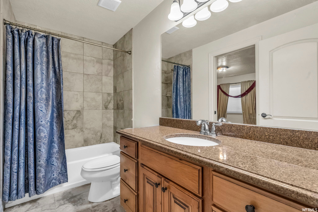 Full bathroom with tile floors, large vanity, toilet, and shower / bath combo