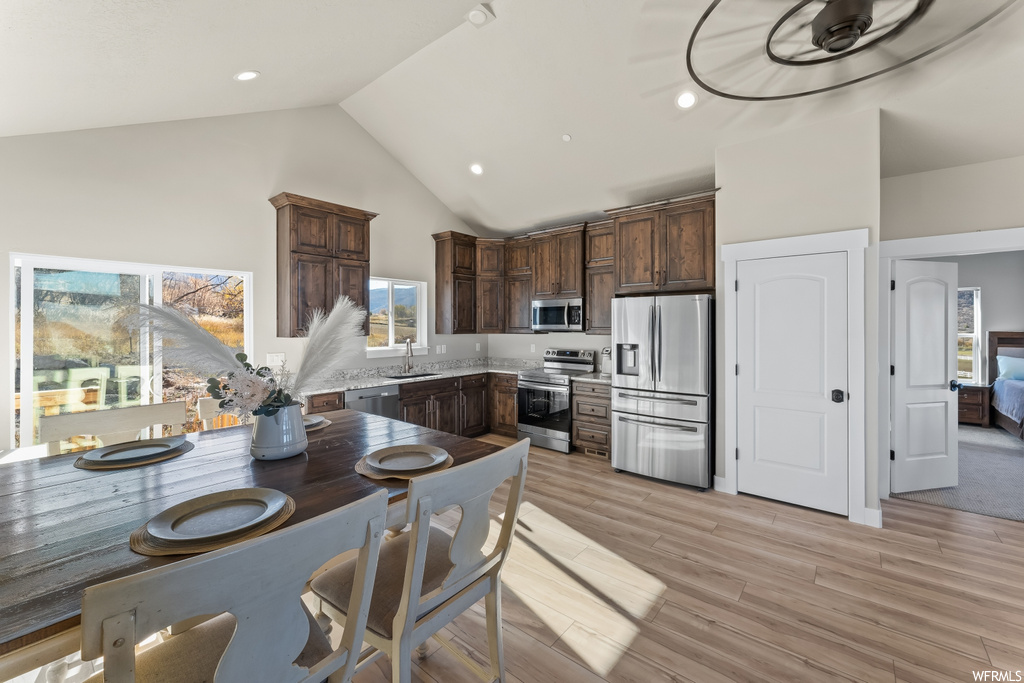 Kitchen featuring sink, high vaulted ceiling, light hardwood / wood-style flooring, appliances with stainless steel finishes, and dark brown cabinetry