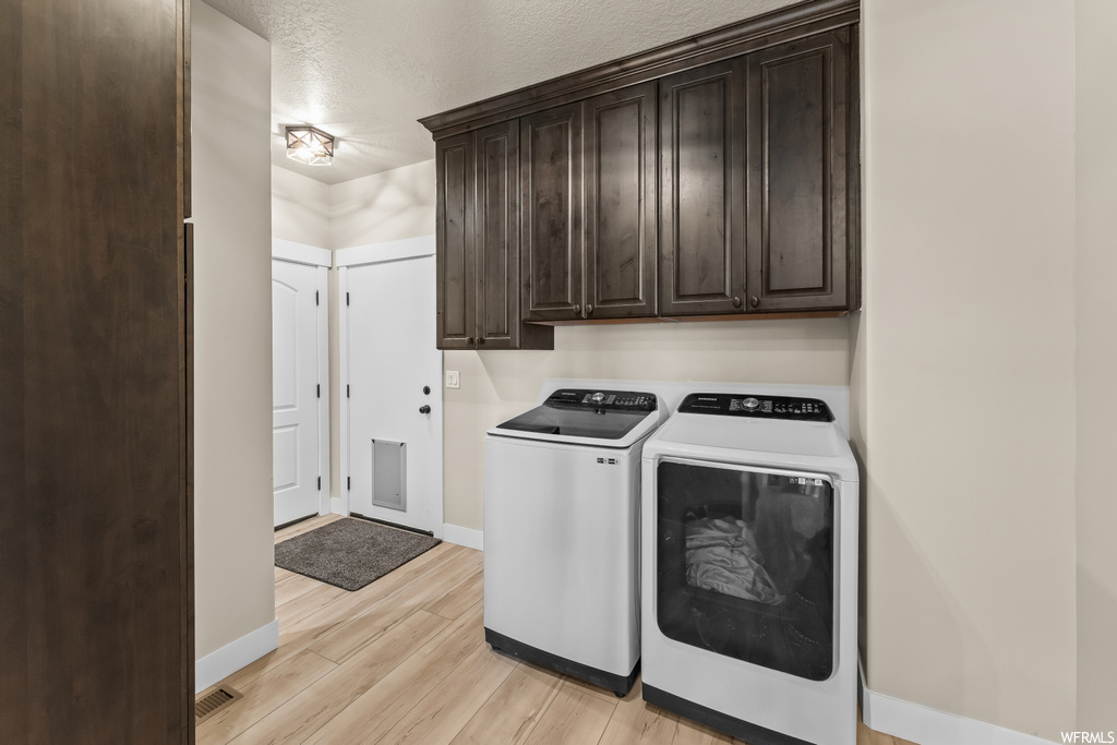 Laundry room featuring washing machine and clothes dryer, light hardwood / wood-style flooring, and cabinets