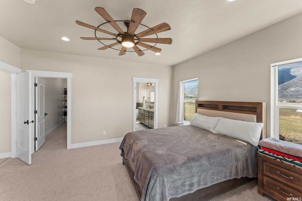 Bedroom with ceiling fan, a spacious closet, ensuite bath, and light colored carpet