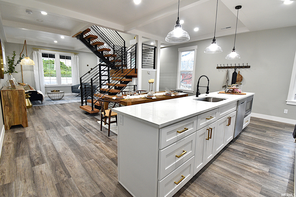 Kitchen with dark hardwood / wood-style flooring, decorative light fixtures, an island with sink, sink, and white cabinetry