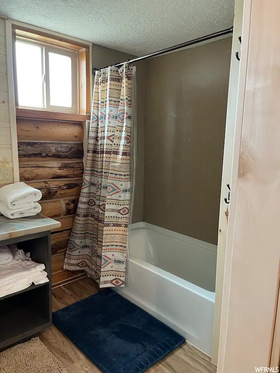 Bathroom featuring shower / bath combo with shower curtain, wood-type flooring, and a textured ceiling