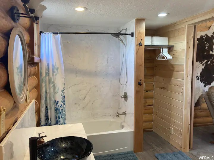 Bathroom featuring wood walls, a textured ceiling, shower / bath combo, and sink