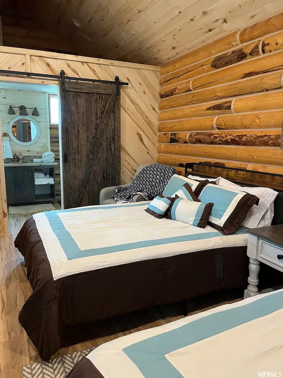 Bedroom with connected bathroom, a barn door, hardwood / wood-style flooring, wooden walls, and wooden ceiling