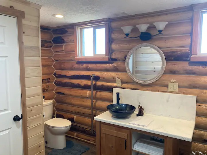 Bathroom with rustic walls, a textured ceiling, toilet, and vanity