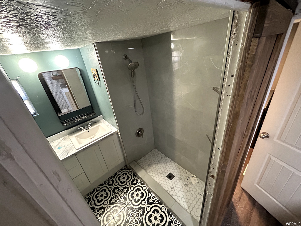 Bathroom with a textured ceiling, vanity with extensive cabinet space, tile flooring, and a tile shower