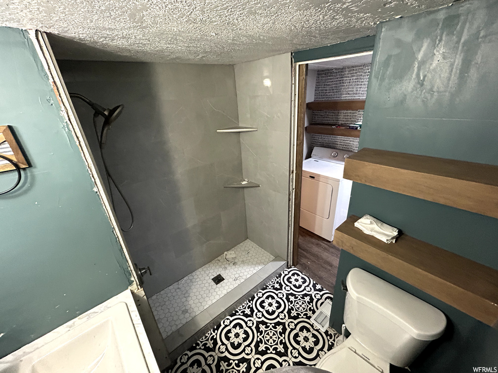 Bathroom featuring washer / dryer, a textured ceiling, hardwood / wood-style flooring, toilet, and a tile shower