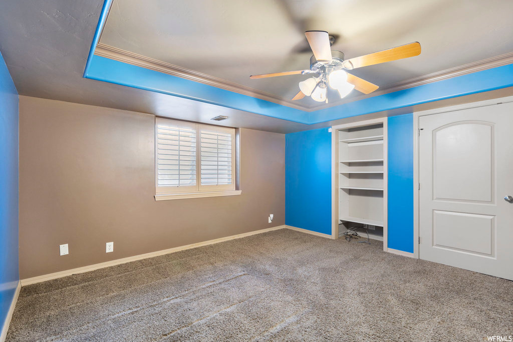 Unfurnished bedroom featuring a tray ceiling, a closet, ceiling fan, crown molding, and carpet floors