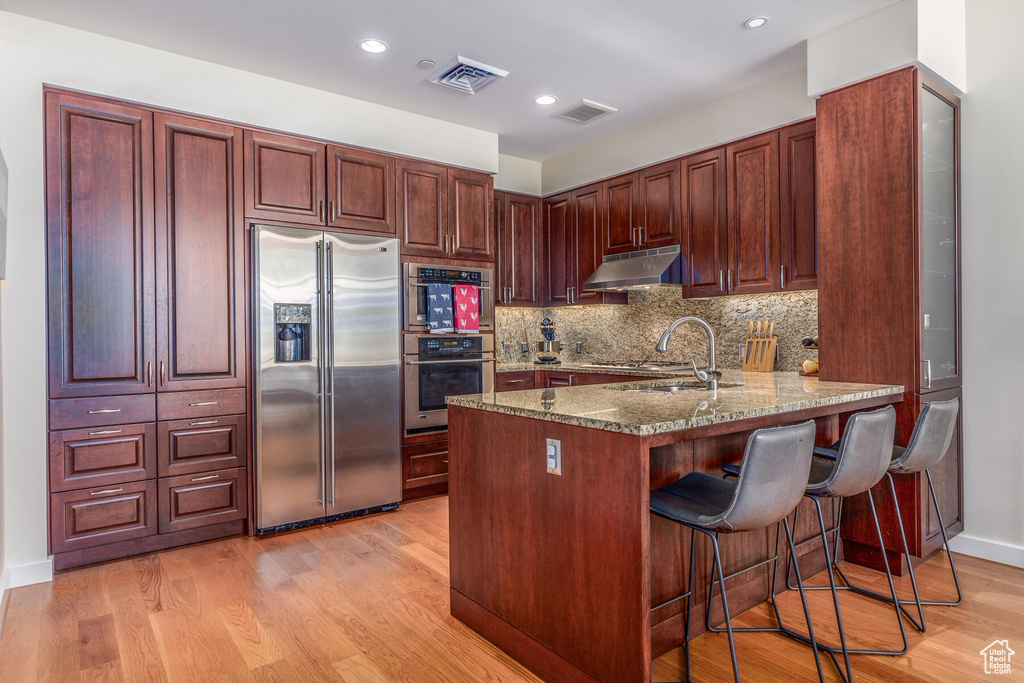 Kitchen with backsplash, light wood-type flooring, light stone countertops, a breakfast bar, and appliances with stainless steel finishes