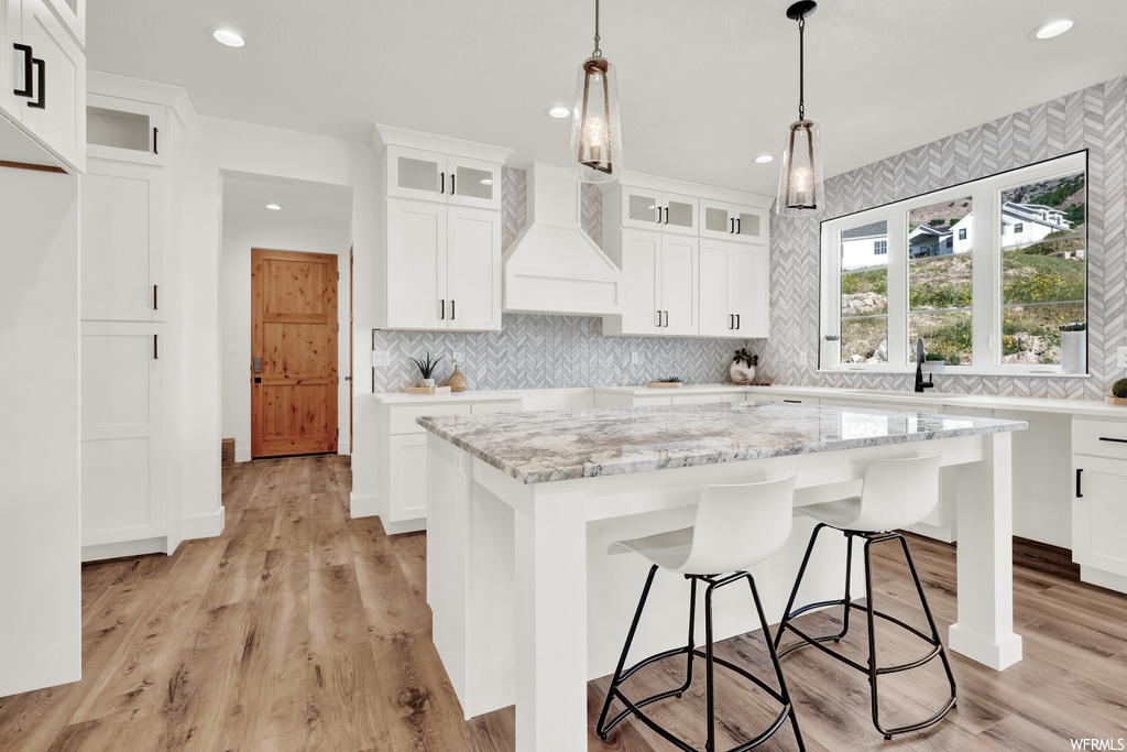 Kitchen with decorative light fixtures, a kitchen island, white cabinets, and custom range hood