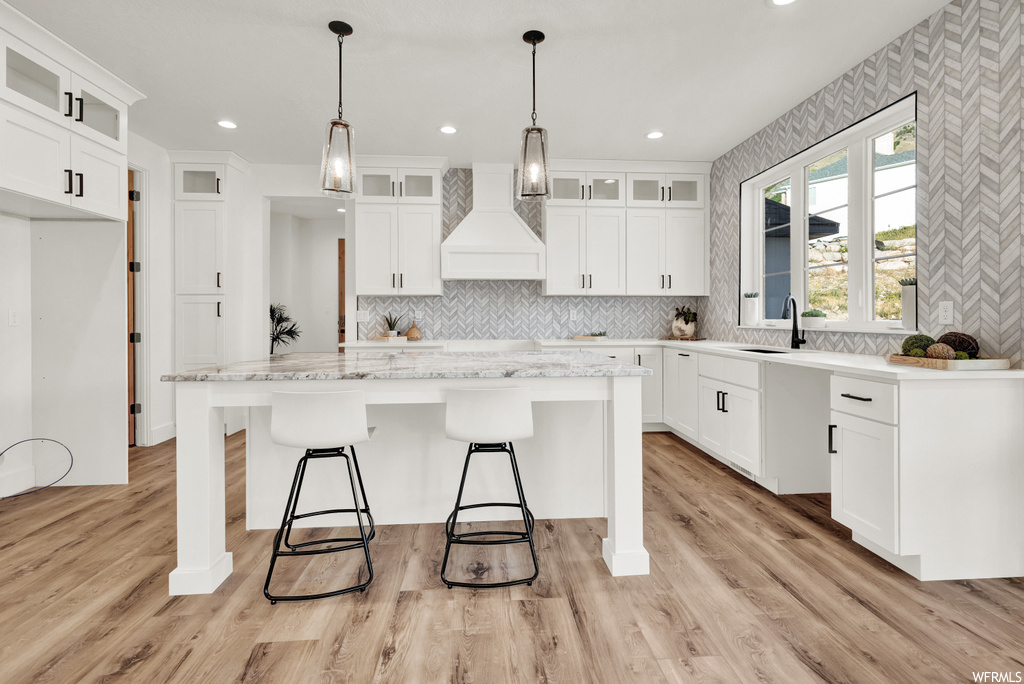 Kitchen with premium range hood, a center island, light hardwood / wood-style floors, white cabinetry, and decorative light fixtures