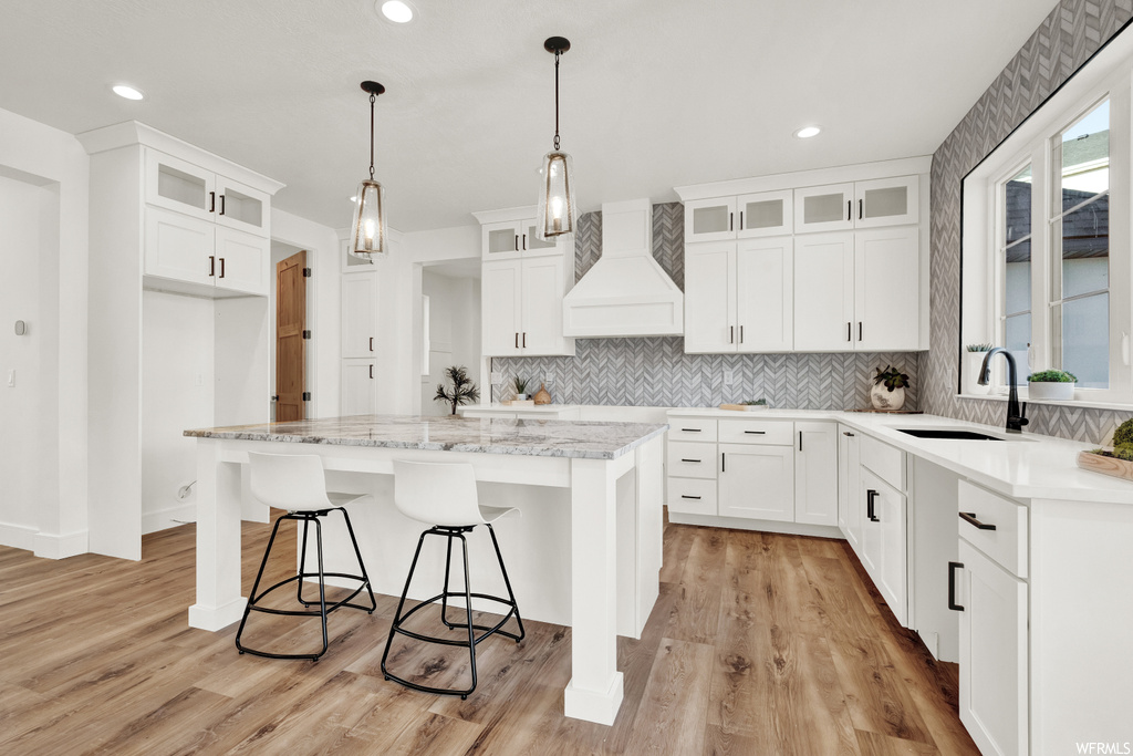 Kitchen with light hardwood / wood-style floors, decorative light fixtures, a kitchen island, white cabinets, and custom range hood