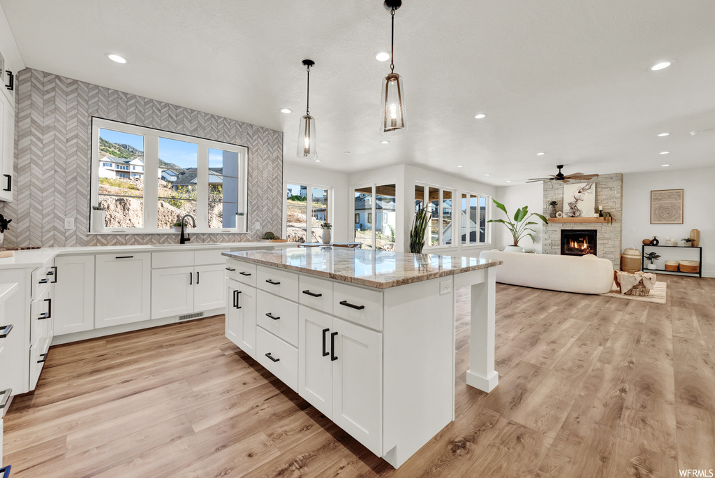 Kitchen with a kitchen island, a fireplace, light stone countertops, light hardwood / wood-style floors, and pendant lighting
