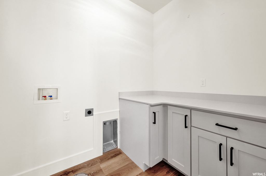 Washroom featuring electric dryer hookup, cabinets, washer hookup, and light hardwood / wood-style flooring