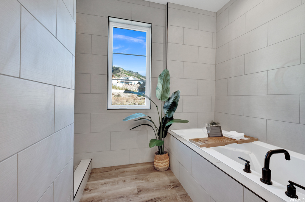 Bathroom featuring tile walls, hardwood / wood-style floors, a bath to relax in, and a baseboard radiator