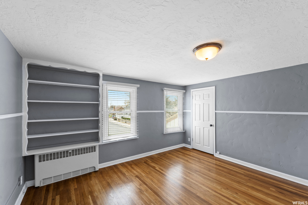 Unfurnished room with wood-type flooring, a textured ceiling, and radiator heating unit
