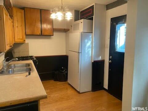 Kitchen featuring sink, an inviting chandelier, white fridge, light hardwood / wood-style floors, and pendant lighting
