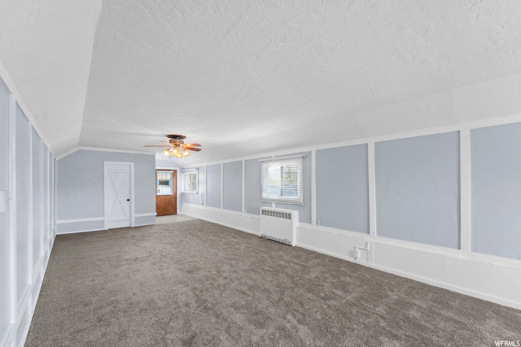 Carpeted spare room with lofted ceiling, a textured ceiling, ceiling fan, and radiator