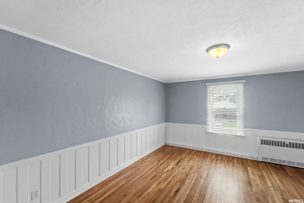 Empty room featuring crown molding, radiator, and wood-type flooring