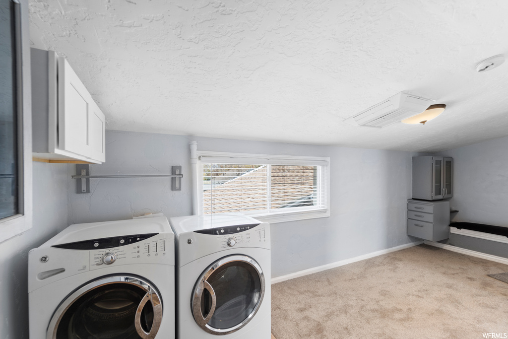 Washroom featuring washing machine and dryer, light carpet, a textured ceiling, and cabinets
