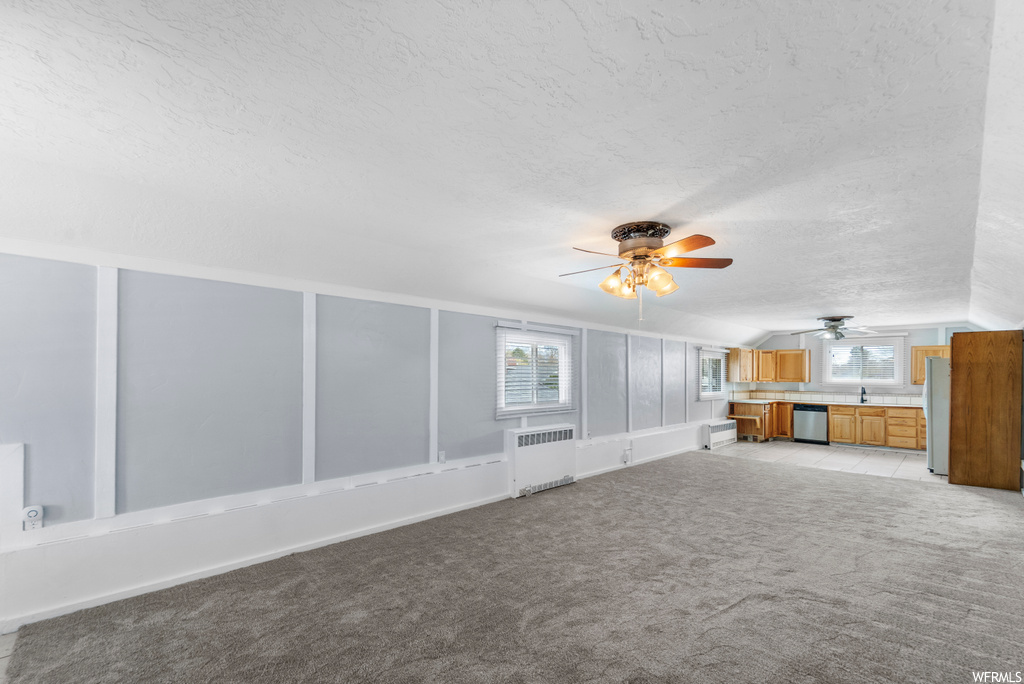 Unfurnished living room featuring ceiling fan, radiator, light colored carpet, and a textured ceiling