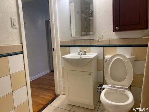 Bathroom with hardwood / wood-style flooring, toilet, and tile walls