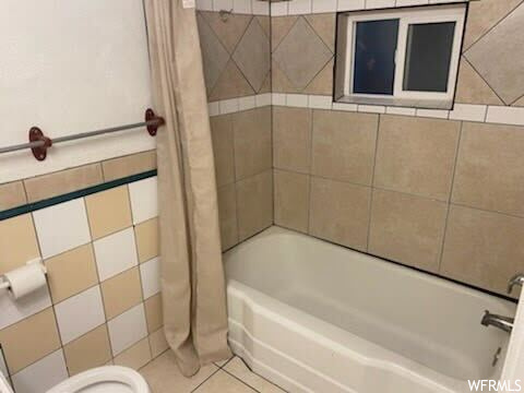 Bathroom with tile walls, shower / bath combo with shower curtain, toilet, and tile floors