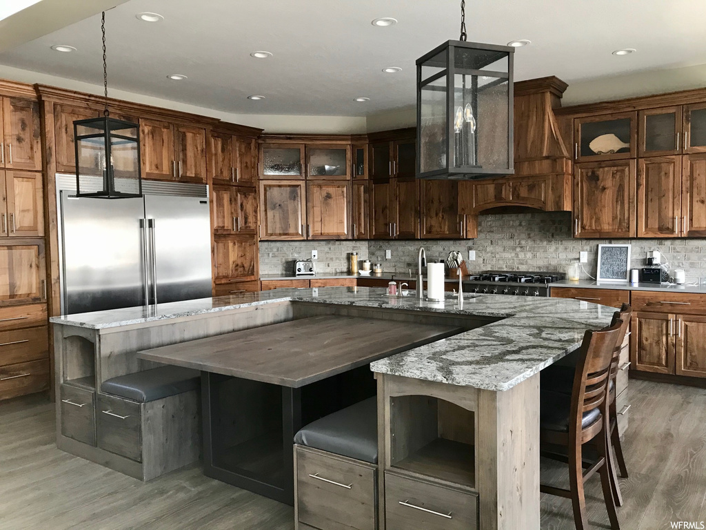 Kitchen with light hardwood / wood-style floors, an island with sink, pendant lighting, and built in refrigerator