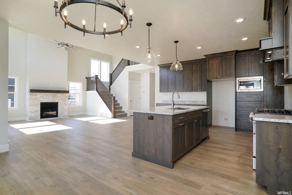 Kitchen with sink, light hardwood / wood-style flooring, a fireplace, a center island with sink, and appliances with stainless steel finishes